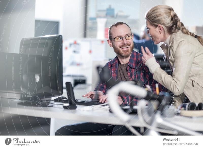 Woman talking to smiling colleague at desk in office working At Work smile speaking offices office room office rooms workplace work place place of work business