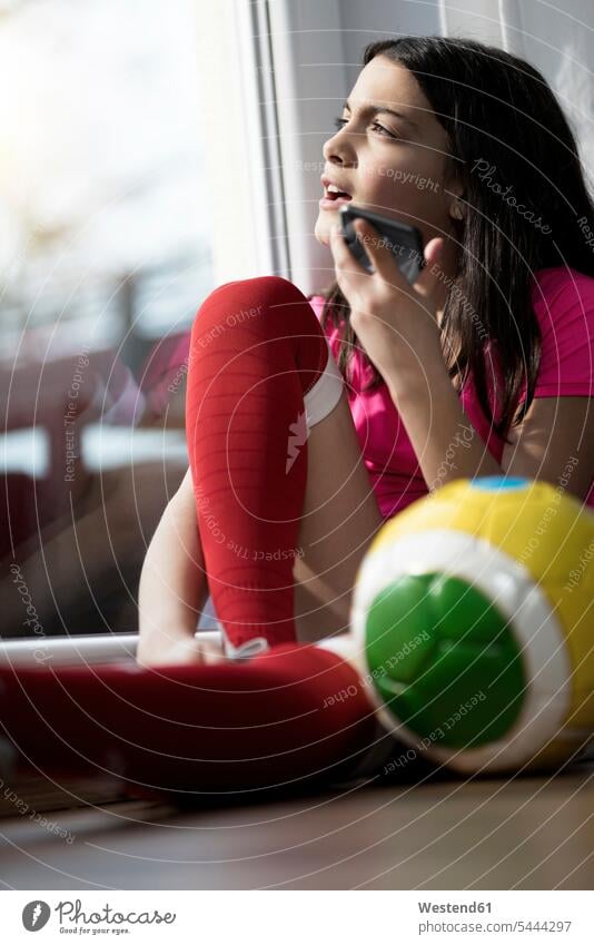 Girl in soccer outfit sitting on floor in living room speaking to someone on her smartphone talking mobile phone mobiles mobile phones Cellphone cell phone