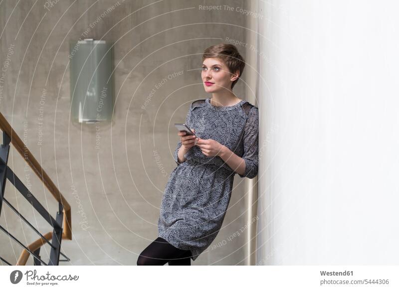 Woman holding cell phone leaning against concrete wall woman females women concrete walls mobile phone mobiles mobile phones Cellphone cell phones Adults