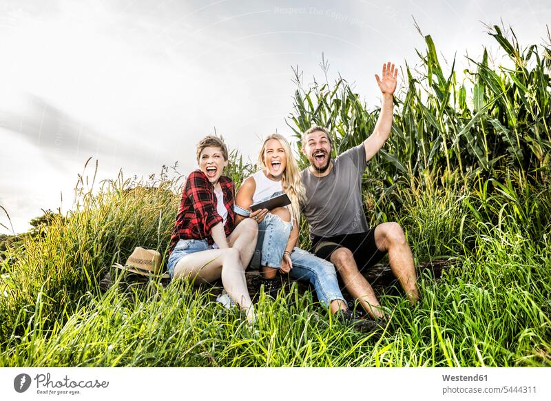 Carefree friends with tablet sitting at a cornfield Field Fields farmland rural country countryside relaxed relaxation mate laughing Laughter Grain field
