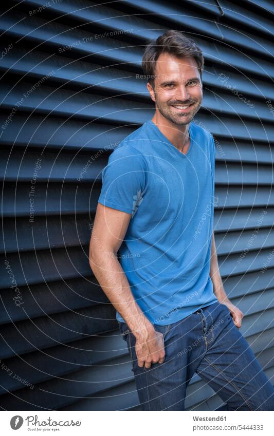 Man standing in front of roller shutter, portrait smiling smile man men males confidence confident leaning portraits leisure free time leisure time Adults