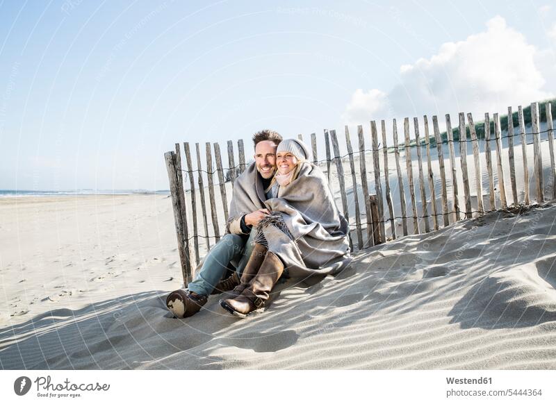 Smiling couple wrapped in blanket on the beach beaches twosomes partnership couples smiling smile people persons human being humans human beings vacation