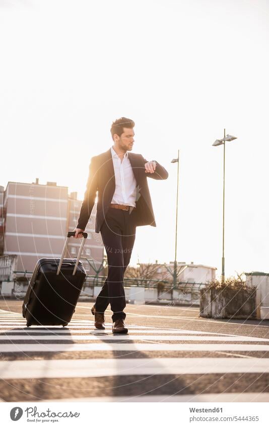 Businessman with rolling suitcase checking the time Business man Businessmen Business men business people businesspeople business world business life walking