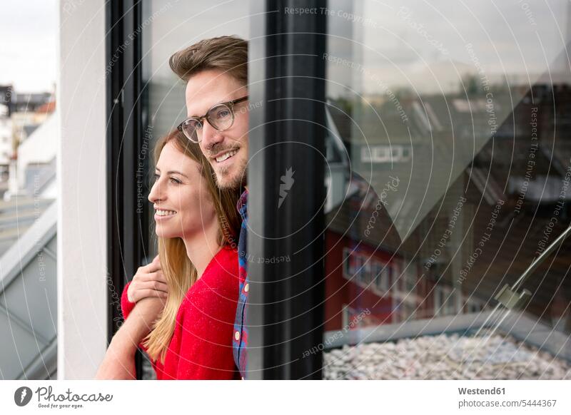 Smiling young couple looking out of window view seeing viewing home at home twosomes partnership couples smiling smile windows people persons human being humans