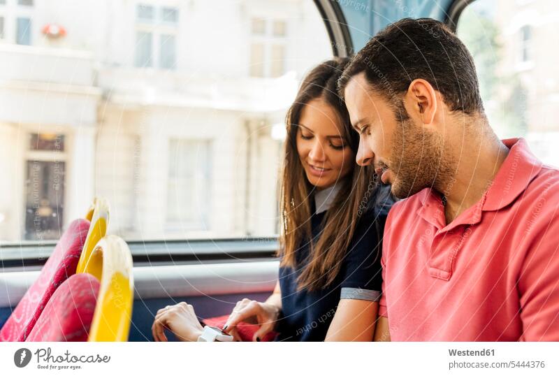 UK, London, couple sitting in a double decker bus using smartwatch smart watch twosomes partnership couples people persons human being humans human beings