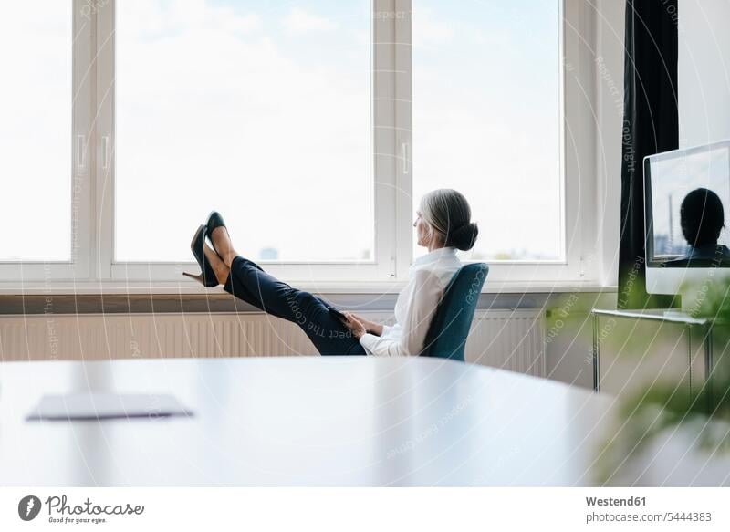 Businesswoman in office sitting at the window looking out windows businesswoman businesswomen business woman business women offices office room office rooms