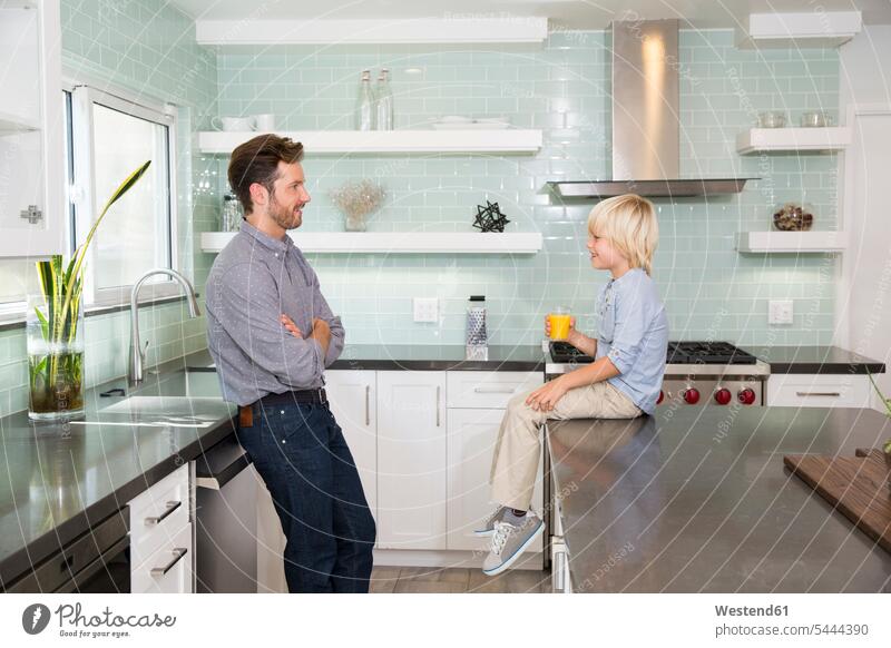 Father and son in kitchen with glass of orange juice Glass Drinking Glasses sons manchild manchildren domestic kitchen kitchens Juice Juices Orange Juice father