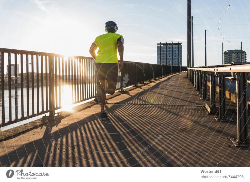 Young athlete jogging on a bridge in the city man men males running headphones headset bridges jogger joggers Sportspeople Sportsman Sportsperson athletes