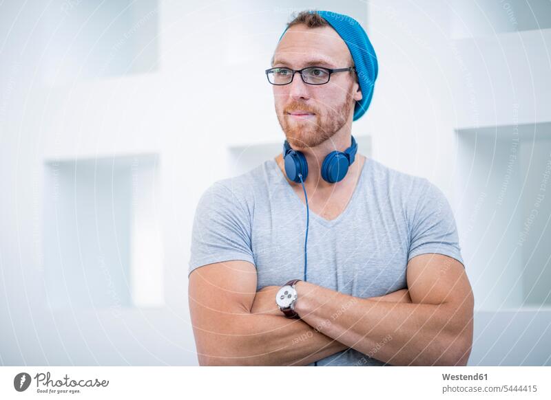 Young man with headphones around his neck looking away with arms crossed young man young men cool attitude composed coolness laid-back thinking Office Offices