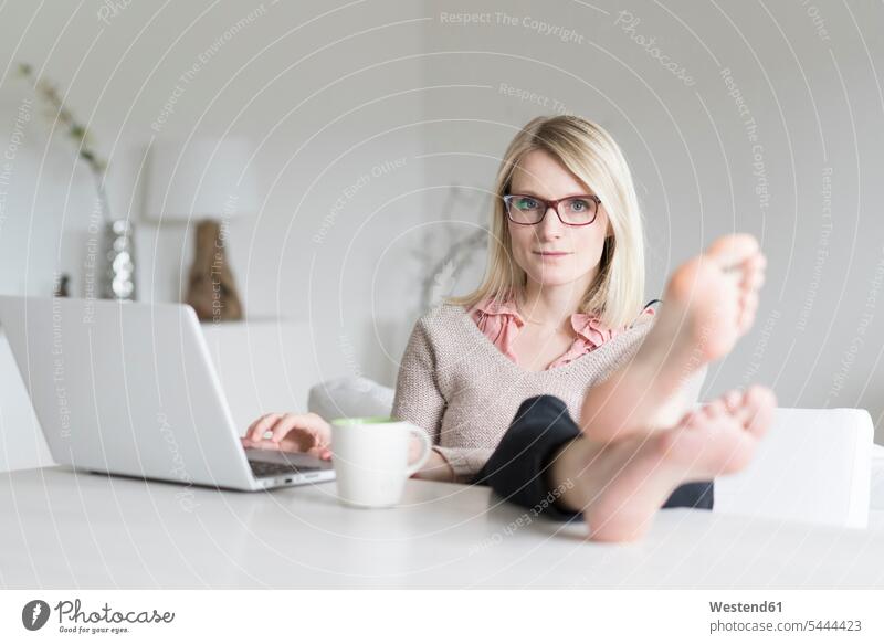 Portrait of blond woman at home sitting at table with feet up portrait portraits laptop Laptop Computers laptops notebook females women computer computers