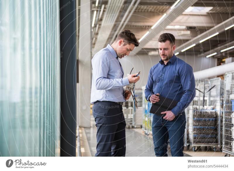 Two men in factory shop floor examining product factories man males colleagues working At Work Adults grown-ups grownups adult people persons human being humans