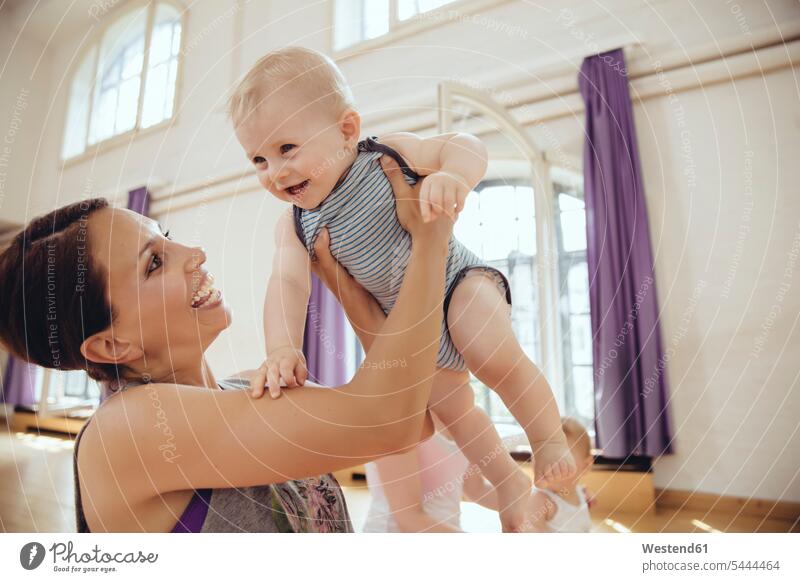 Happy mother lifting up her baby in an exercise room exercising training practising Fun having fun funny mommy mothers ma mummy mama infants nurselings babies