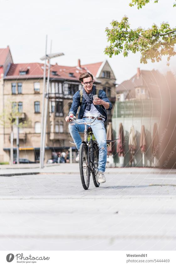 Smiling young man with bicycle in the city looking at cell phone men males bikes bicycles smiling smile mobile phone mobiles mobile phones Cellphone cell phones