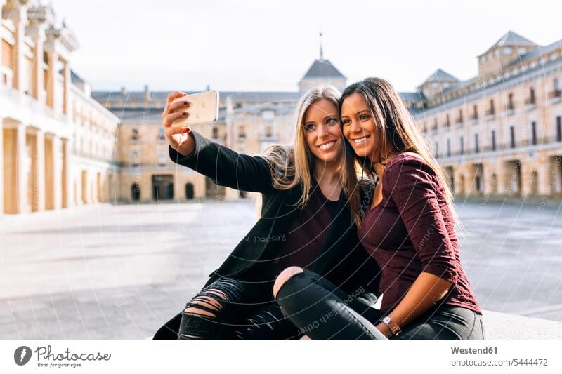 Two smiling young women on urban square taking a selfie smile mobile phone mobiles mobile phones Cellphone cell phone cell phones Selfie Selfies woman females