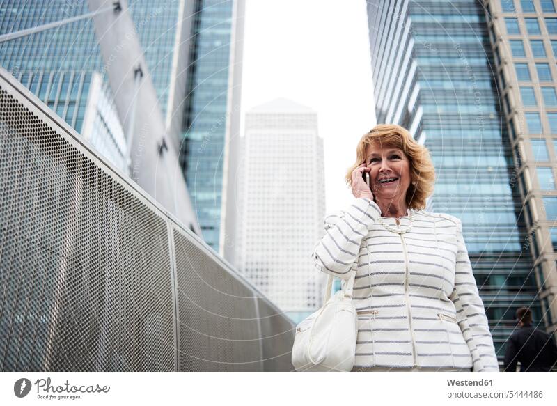 UK, London, smiling senior businesswoman on the phone in the city businesswomen business woman business women portrait portraits females call telephoning
