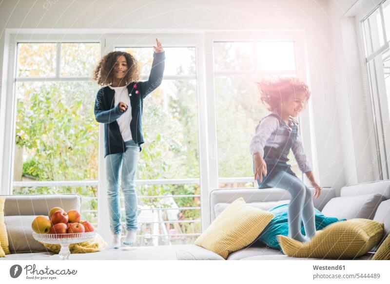Happy girls jumping and hopping on couch settee sofa sofas couches settees females Leaping bounce bouncing bounding sister sisters laughing Laughter child