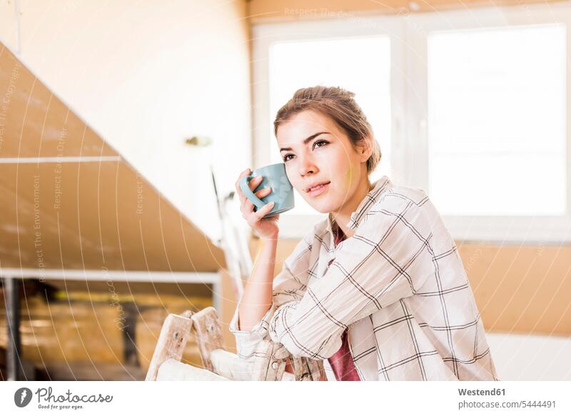 Young woman holding coffee cup, thinking of renovation of her new home young women young woman home ownership private owned home renovate refurbish refurbishing
