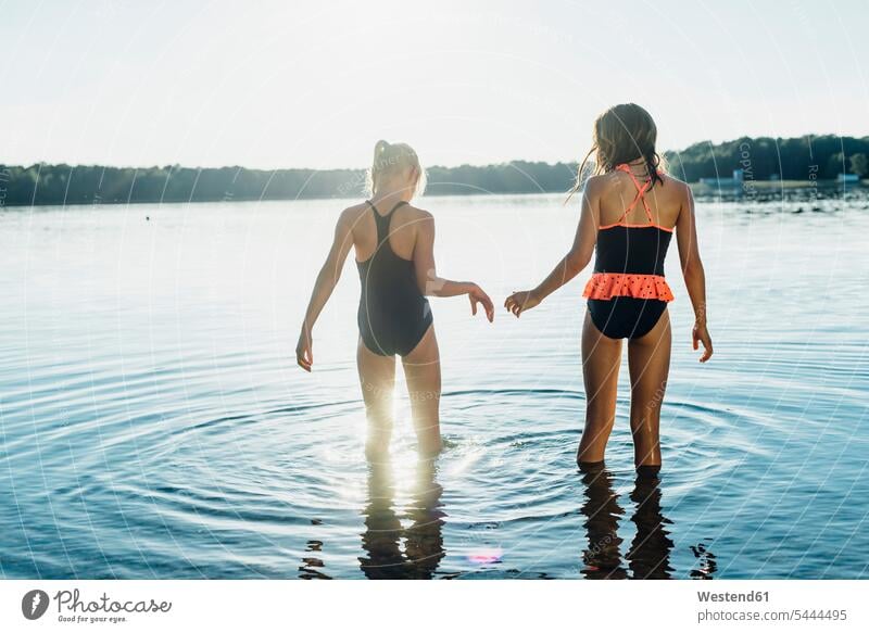 Back view of two friends wearing swimsuits standing at lakeshore girl females girls female friends child children kid kids people persons human being humans