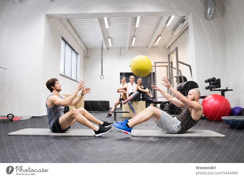 Two athletes exercising with ball in gym with training partners watching exercise practising gyms Health Club balls throwing fitness sport sports Fitness