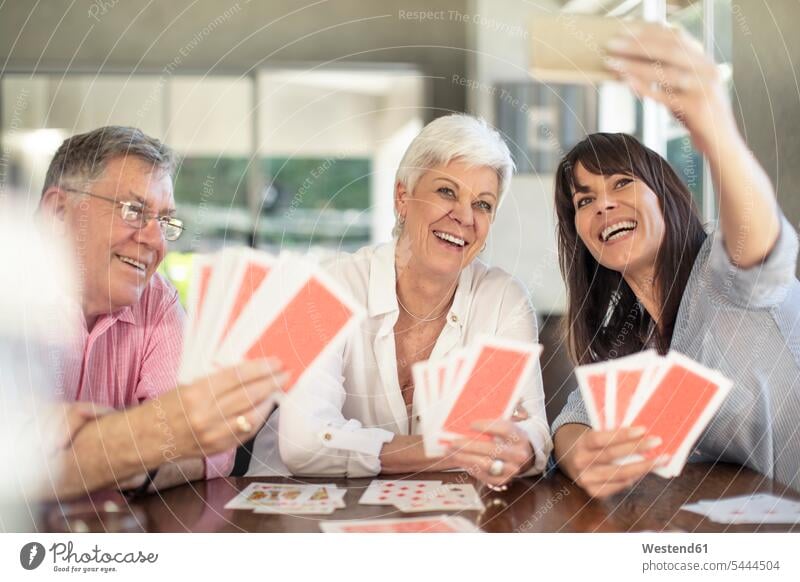 Happy senior couple playing cards and taking a selfie with daughter at home daughters happiness happy Selfie Selfies senior men senior man elder man elder men