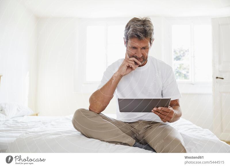 Portrait of mature man with digital tablet in bedroom Domestic Bedroom men males reading sitting Seated digitizer Tablet Computer Tablet PC Tablet Computers