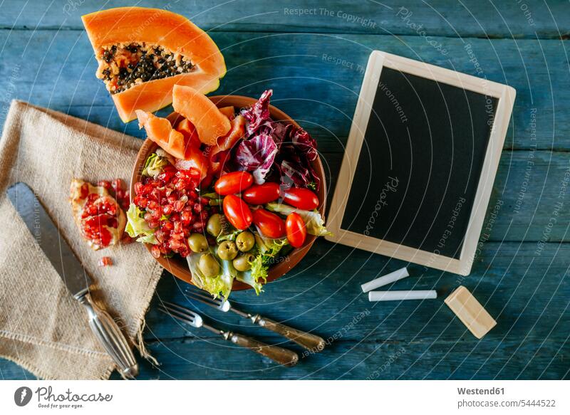 Papaya salad, pomegranate, lettuce, tomato, olives and endive with slate, on blue wood food and drink Nutrition Alimentation Food and Drinks salad bowl
