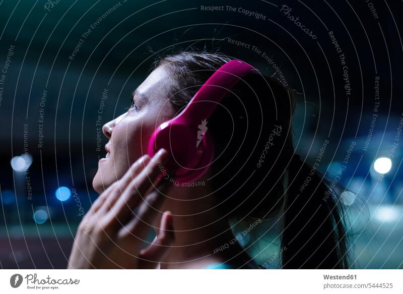 Happy young woman with pink headphones listening to music in modern urban setting at night exercising exercise training practising young women on the phone call