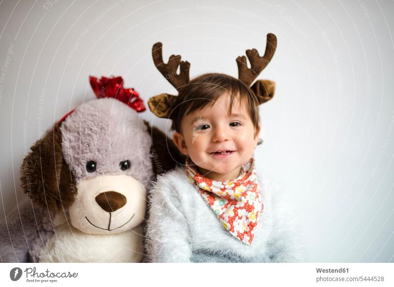 Portrait of happy baby girl with reindeer antlers headband beside her toy dog happiness portrait portraits soft toy soft toys Antler Antlers caribu caribou