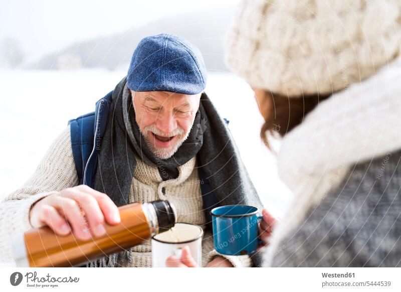 Senior couple having a break with hot beverages in snow senior couple elder couples senior couples adult couple adult couples twosomes partnership people