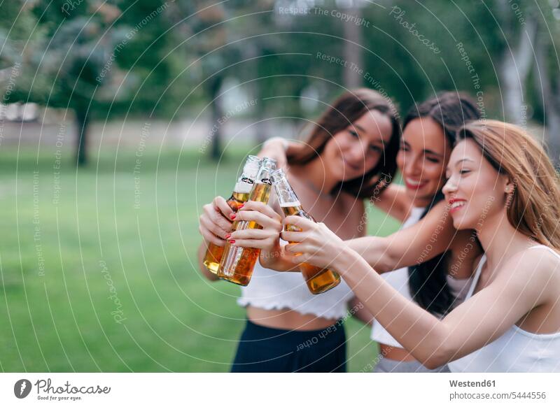 Friends in a park clinking beer bottles holding toasting cheers Beer Beers Ale female friends parks Alcohol alcoholic beverage Alcoholic Drink Alcoholic Drinks
