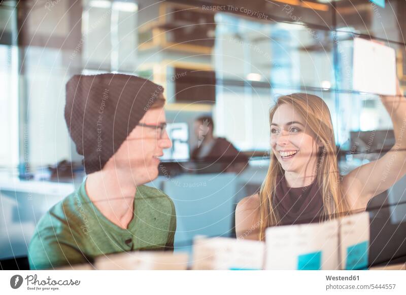 Young man and woman working together in an office colleagues Brainstorming glass pane glass panes At Work Office Offices window windows Female Colleague note