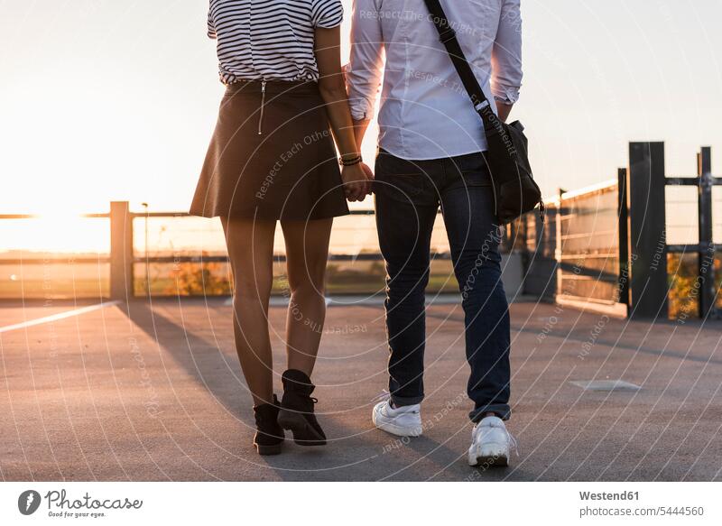 Young couple walking hand in hand on parking level at sunset going sunsets sundown twosomes partnership couples atmosphere atmospheric mood moody