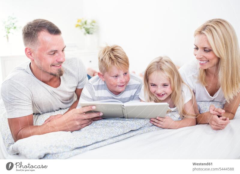 Family lying in bed reading book together books family families smiling smile beds people persons human being humans human beings home at home 6-7 years