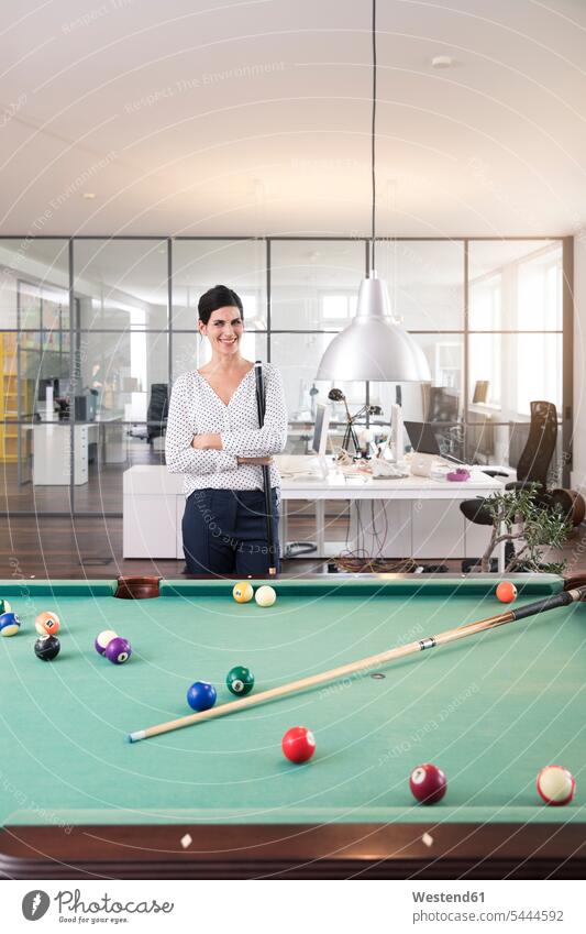 Businesswoman standing at pool table, playing billard, smiling strategy strategic Strategies billiards game games career relaxation relaxed relaxing