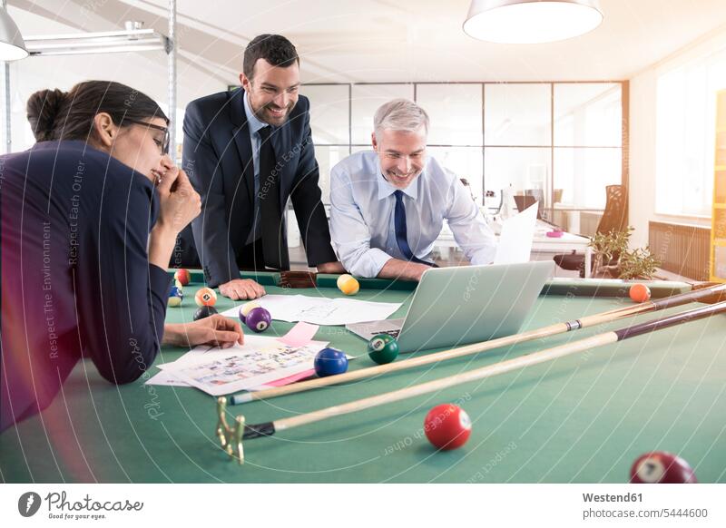Business people standing at pool table with laptop, discussing investment strategy business people businesspeople Laptop Computers laptops notebook strategic