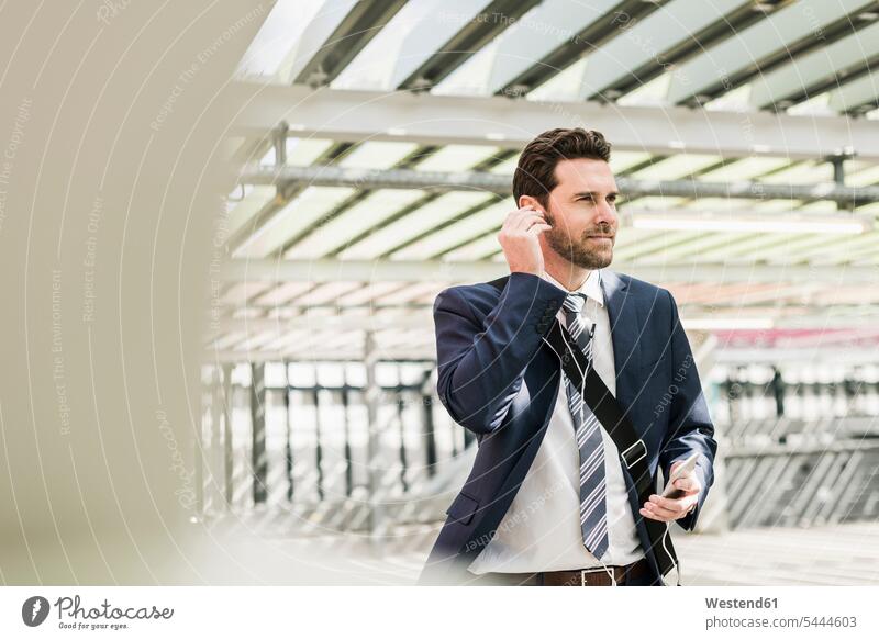 Businessman standing on parking level making a call using earphones on the phone telephoning On The Telephone calling Smartphone iPhone Smartphones ear phone
