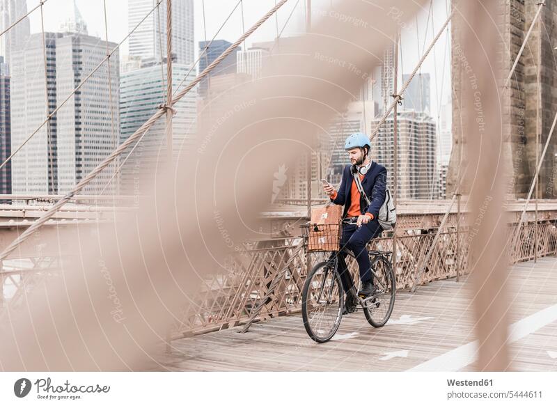 USA, New York City, man on bicycle on Brooklyn Bridge using cell phone men males bridge bridges bikes bicycles mobile phone mobiles mobile phones Cellphone