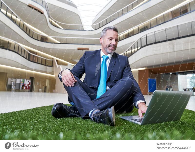Businesssman sitting on synthetic turf using laptop Businessman Business man Businessmen Business men Seated Laptop Computers laptops notebook smiling smile