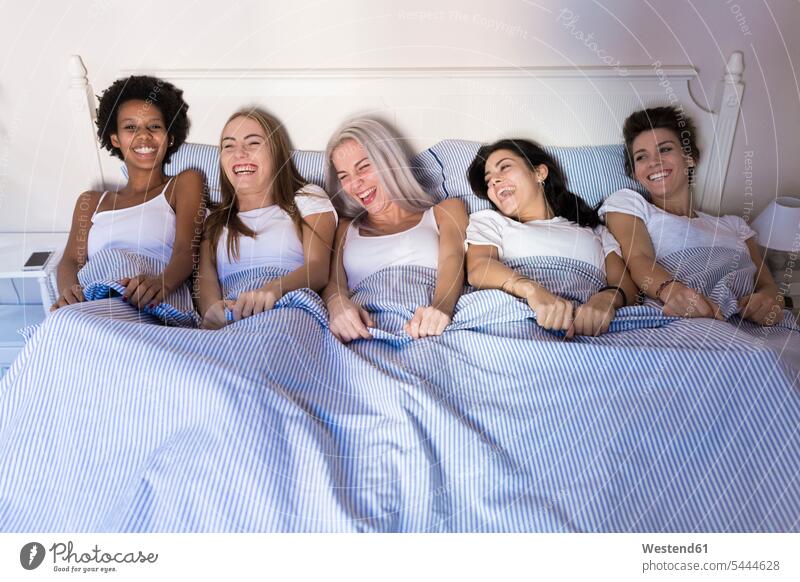 Portrait of happy female friends lying in bed side by side portrait portraits laughing Laughter laying down lie lying down woman females women beds positive