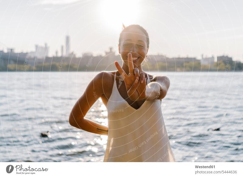 Young woman in Brooklyn standing at East River giving victory sign females women V sign v-sign Joy enjoyment pleasure Pleasant delight carefree attractive