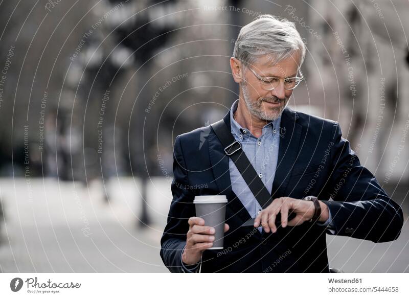 Grey-haired businessman in the city looking at watch holding coffee to go mobile phone mobiles mobile phones Cellphone cell phone cell phones Coffee Businessman