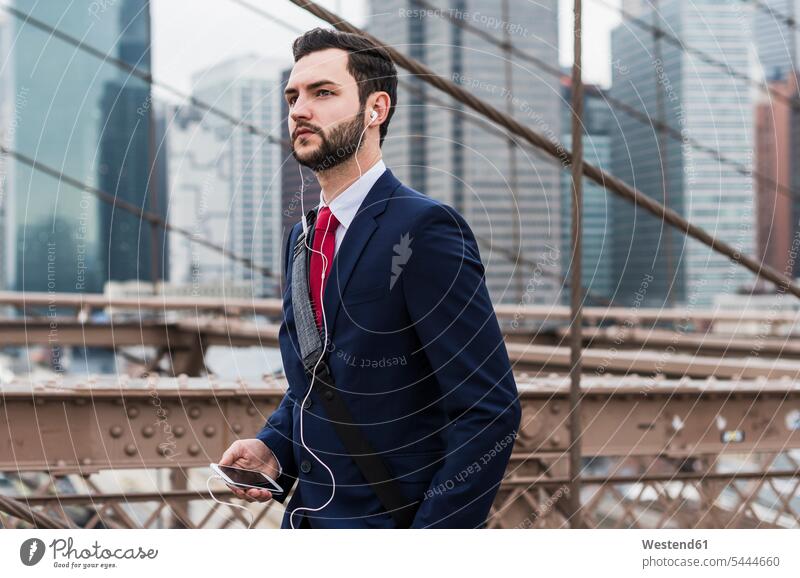 USA, New York City, businessman with cell phone and earbuds on Brooklyn Bridge New York State Businessman Business man Businessmen Business men bridge bridges