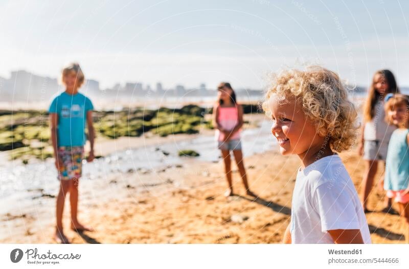 Happy little boy on the beach with other children standing in the background beaches looking watching boys males playing view seeing viewing kid kids people