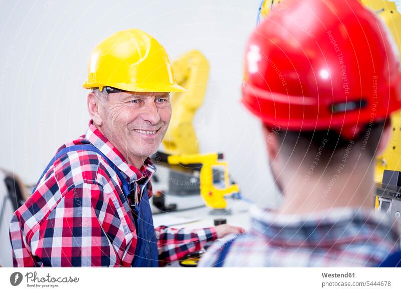Man in factory wearing hard hat smiling at colleague factories colleagues industry industrial producing making technician technicians business business world