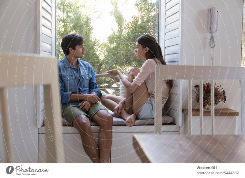 Young couple talking on windowsill relaxed relaxation sitting Seated speaking twosomes partnership couples relaxing people persons human being humans