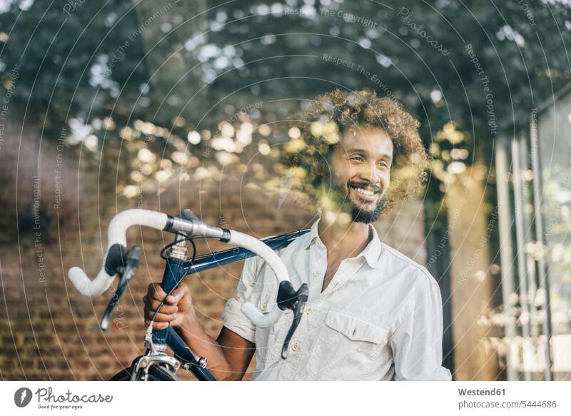 Smiling young man carrying bicycle smiling smile men males bikes bicycles Adults grown-ups grownups adult people persons human being humans human beings