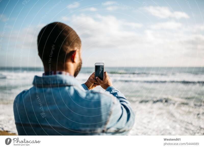Back view of young man taking pictures of the sea Smartphone iPhone Smartphones photographing mobile phone mobiles mobile phones Cellphone cell phone