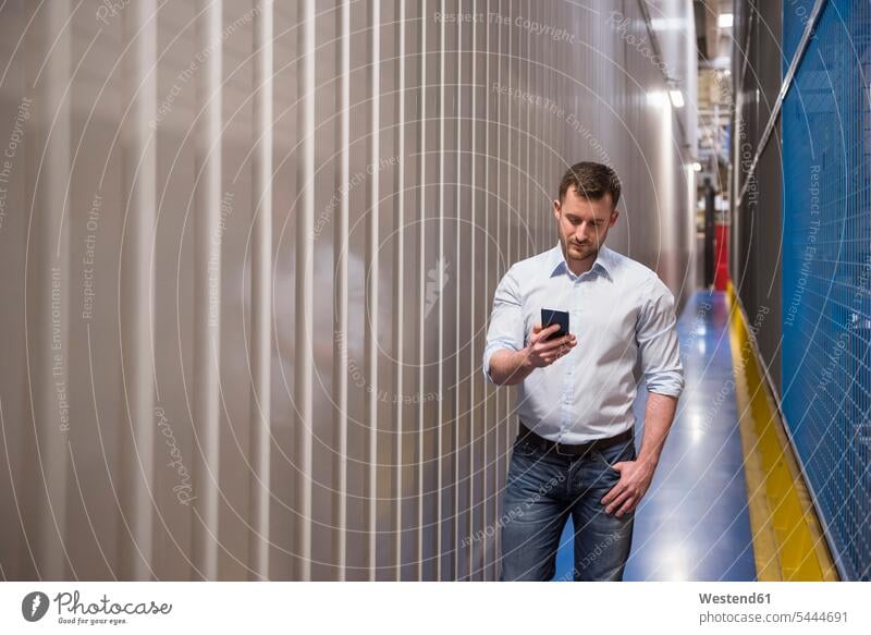 Man in passageway in a factory looking at cell phone Businessman Business man Businessmen Business men mobile phone mobiles mobile phones Cellphone cell phones