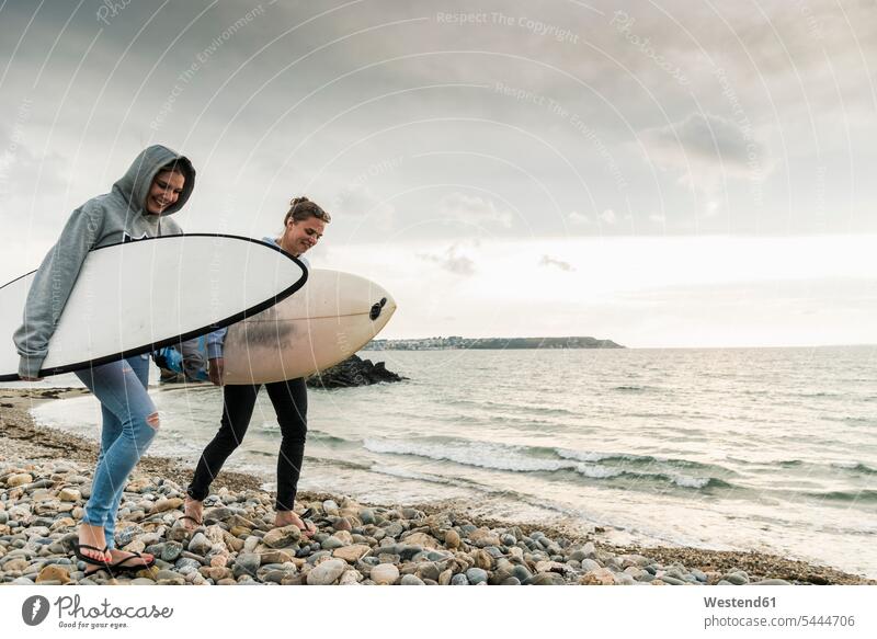 Happy friends with surfboard walking on stony beach female friends beaches happiness happy surfboards going mate friendship surfing surf ride surf riding