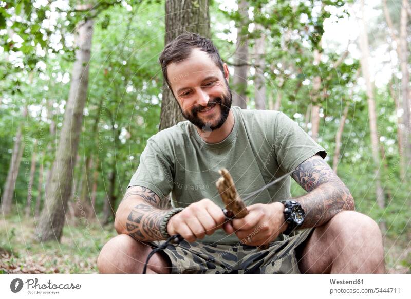 Smiling man carving in the forest woods forests men males knife knives smiling smile tattoo tattoos Carving whittling Adults grown-ups grownups adult people